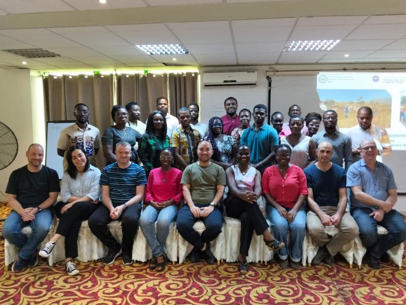 26 people from Pirbright, Roslin and Ghana posing for group photo. Nine people at the front are sat on chairs while the remaining group is stood behind them