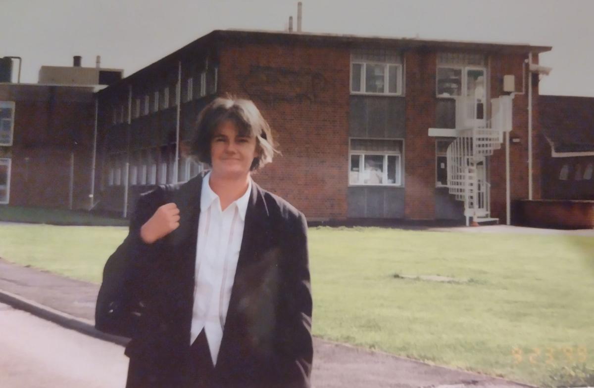 Old photo of young Linda Dixon stood in front of a brick building with a green lawn