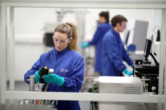 Three scientists in blue labcoats branded with CPI. One is holding a pipette while two others in the background are looking at computer screens.