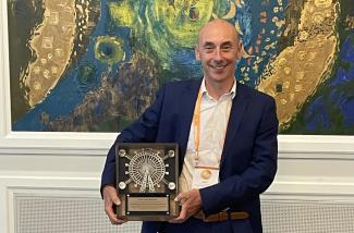 Gary Entrican holding the award in front of a large painting